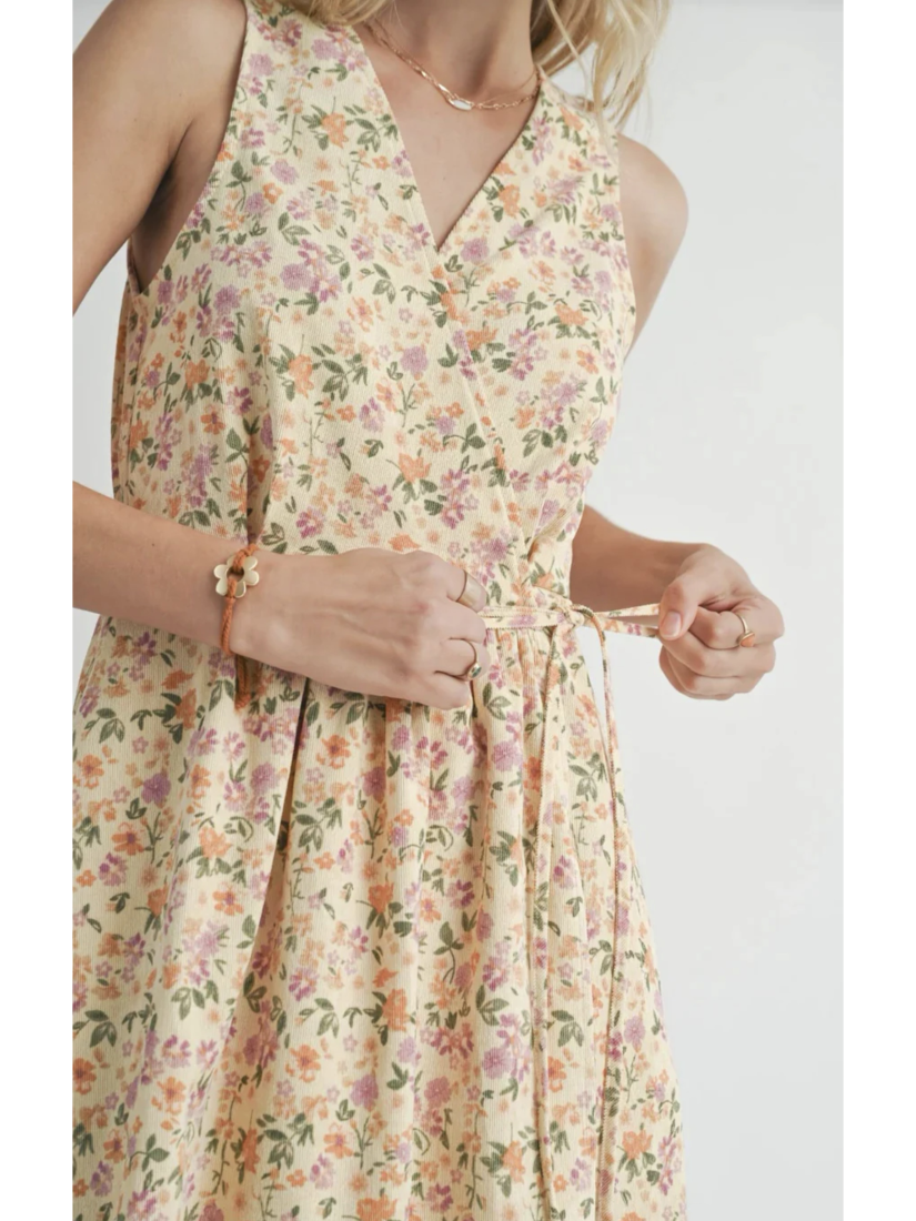A midi length sleeveless dress with a v-neck design, featuring a floral pattern. The model is wearing the dress with flat sandals.