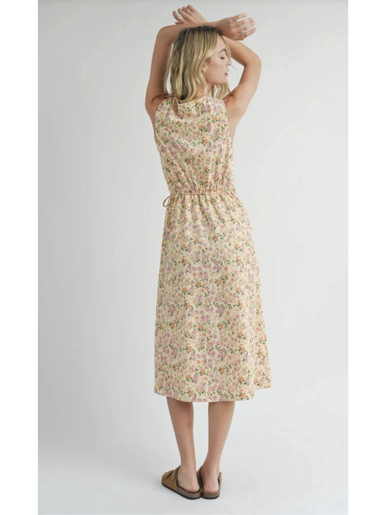 A midi length sleeveless dress with a v-neck design, featuring a floral pattern. The model is wearing the dress with flat sandals.