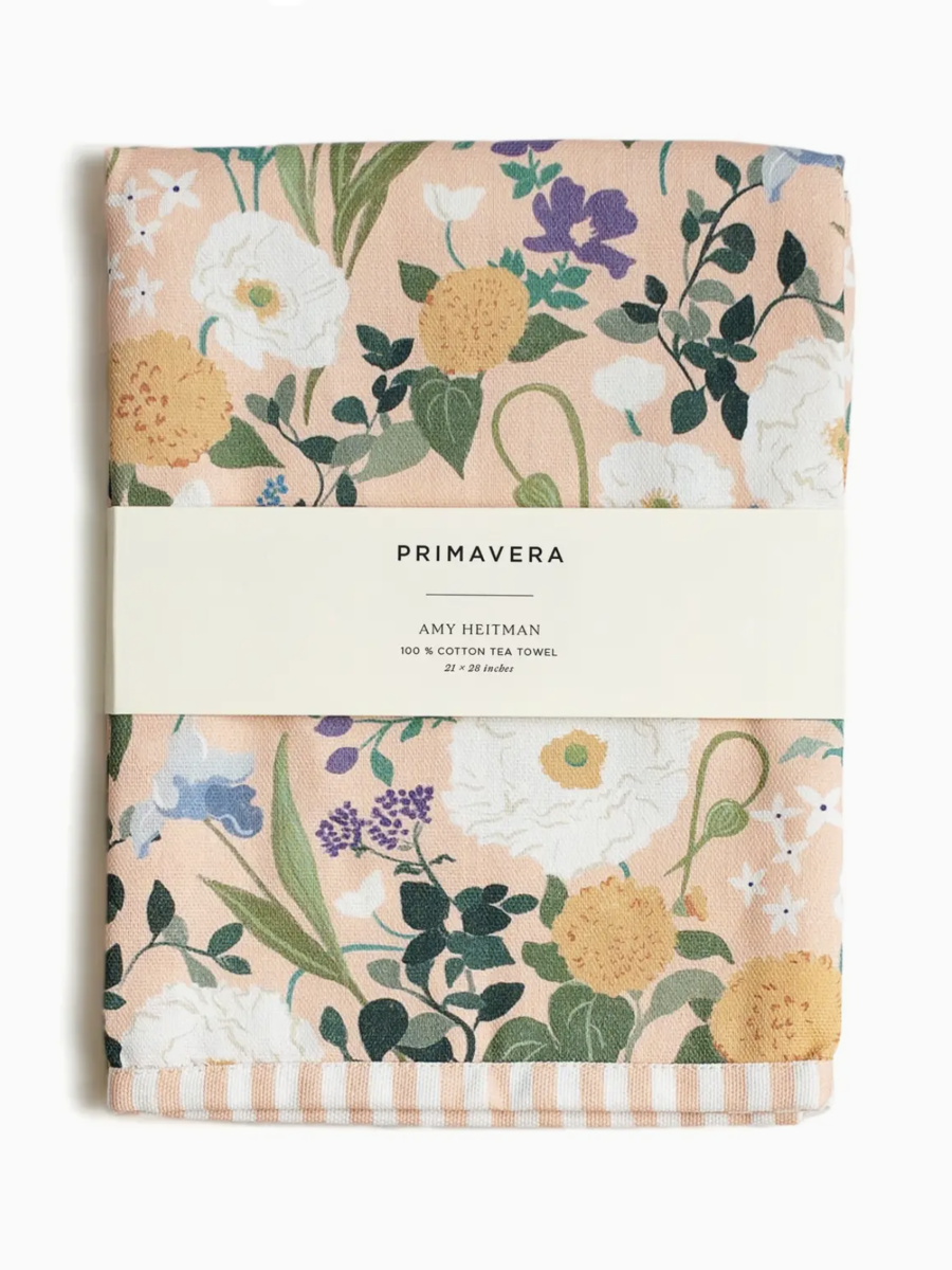 Watercolor floral tea towel with red poppies, yellow daisies, and blue flowers hanging in a bright kitchen.
