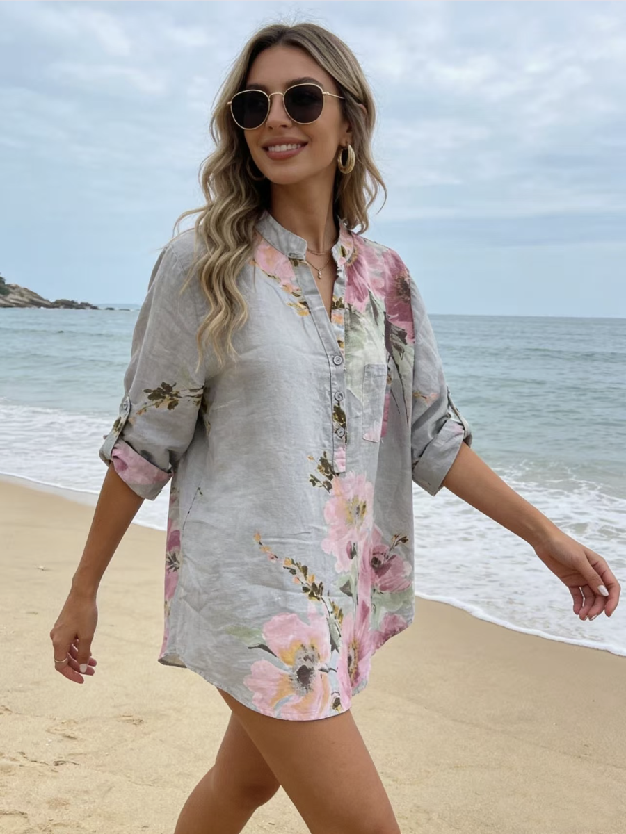Woman in a floral blouse walking on a beach with ocean and sky in the background