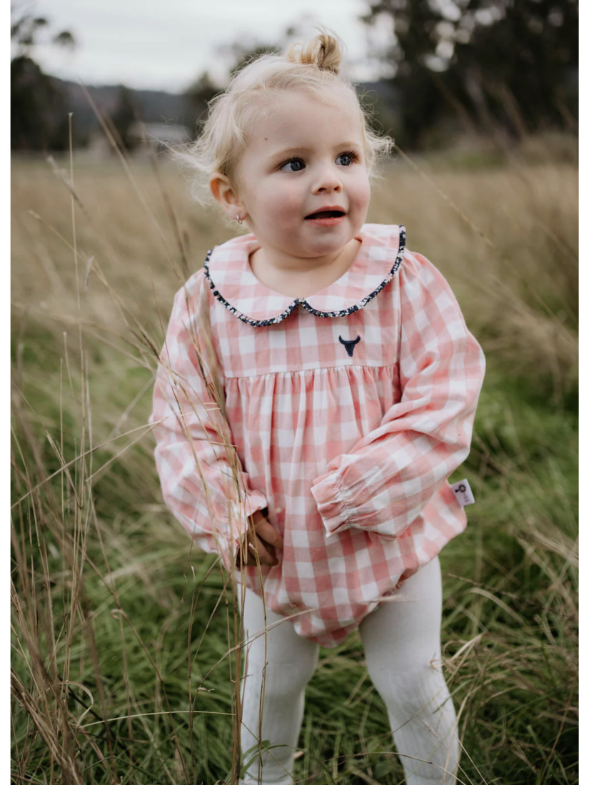 Child wearing a pink checkered dress standing in tall grass