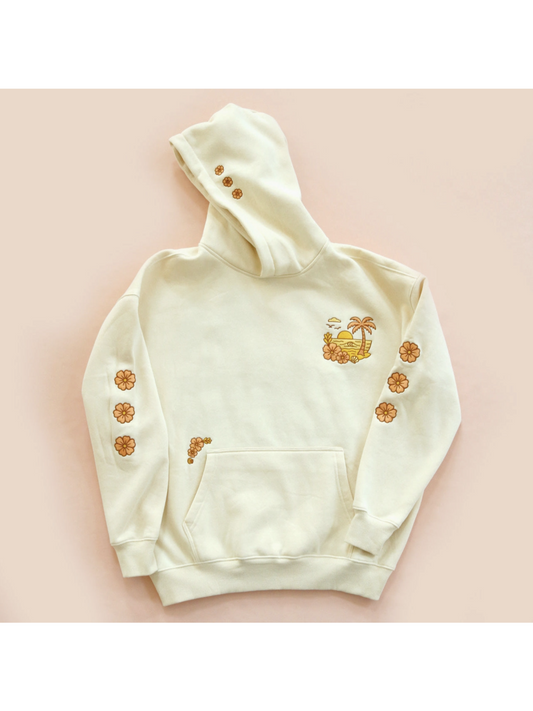 Cozy hoodie featuring a detailed embroidery of a coastal sunset over waves, designed for a whimsical and relaxed slow-living aesthetic.