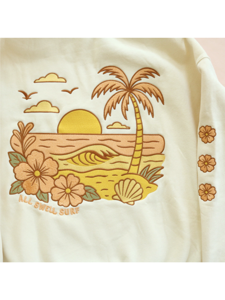 Cozy hoodie featuring a detailed embroidery of a coastal sunset over waves, designed for a whimsical and relaxed slow-living aesthetic.