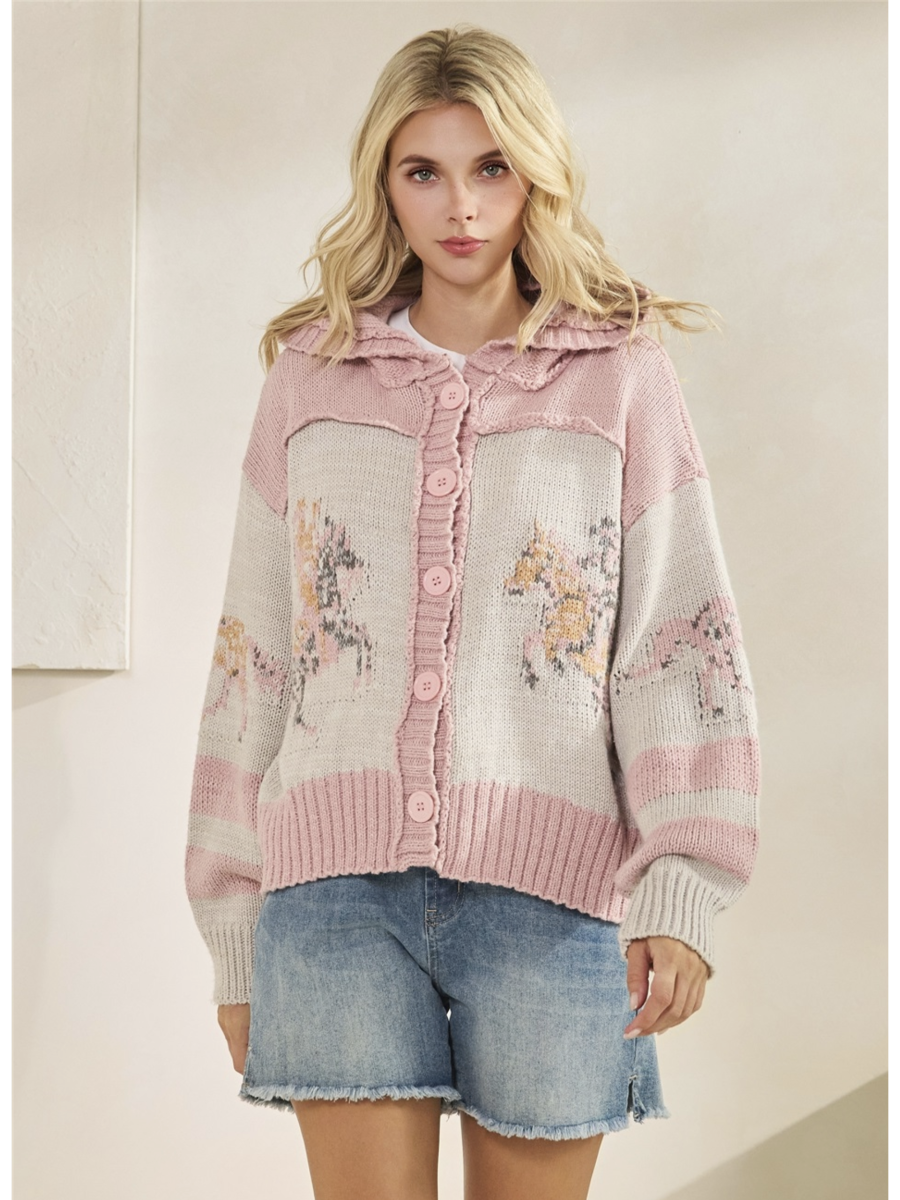 Woman wearing a pink and beige cardigan with unicorn designs on a plain background