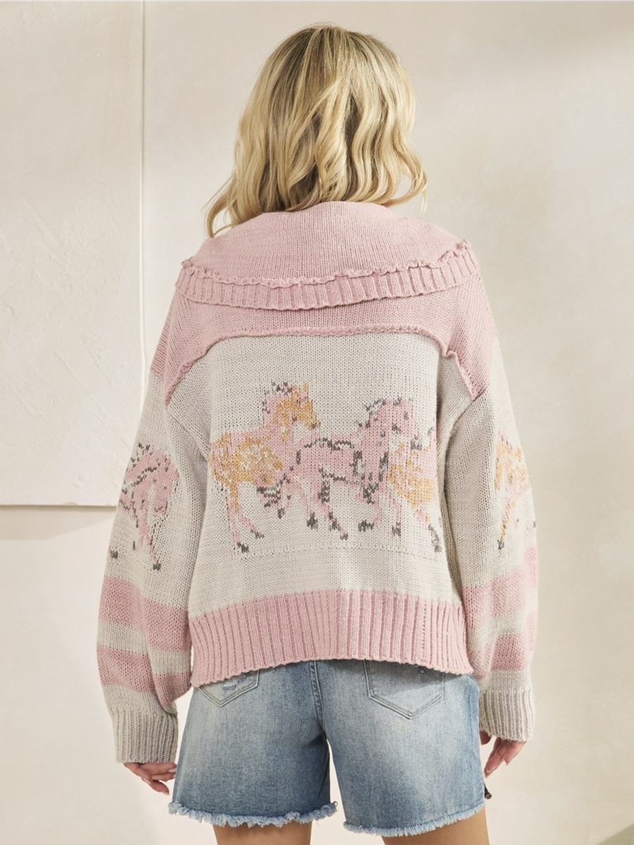 Person wearing a pink and gray sweater with horse designs on a plain background