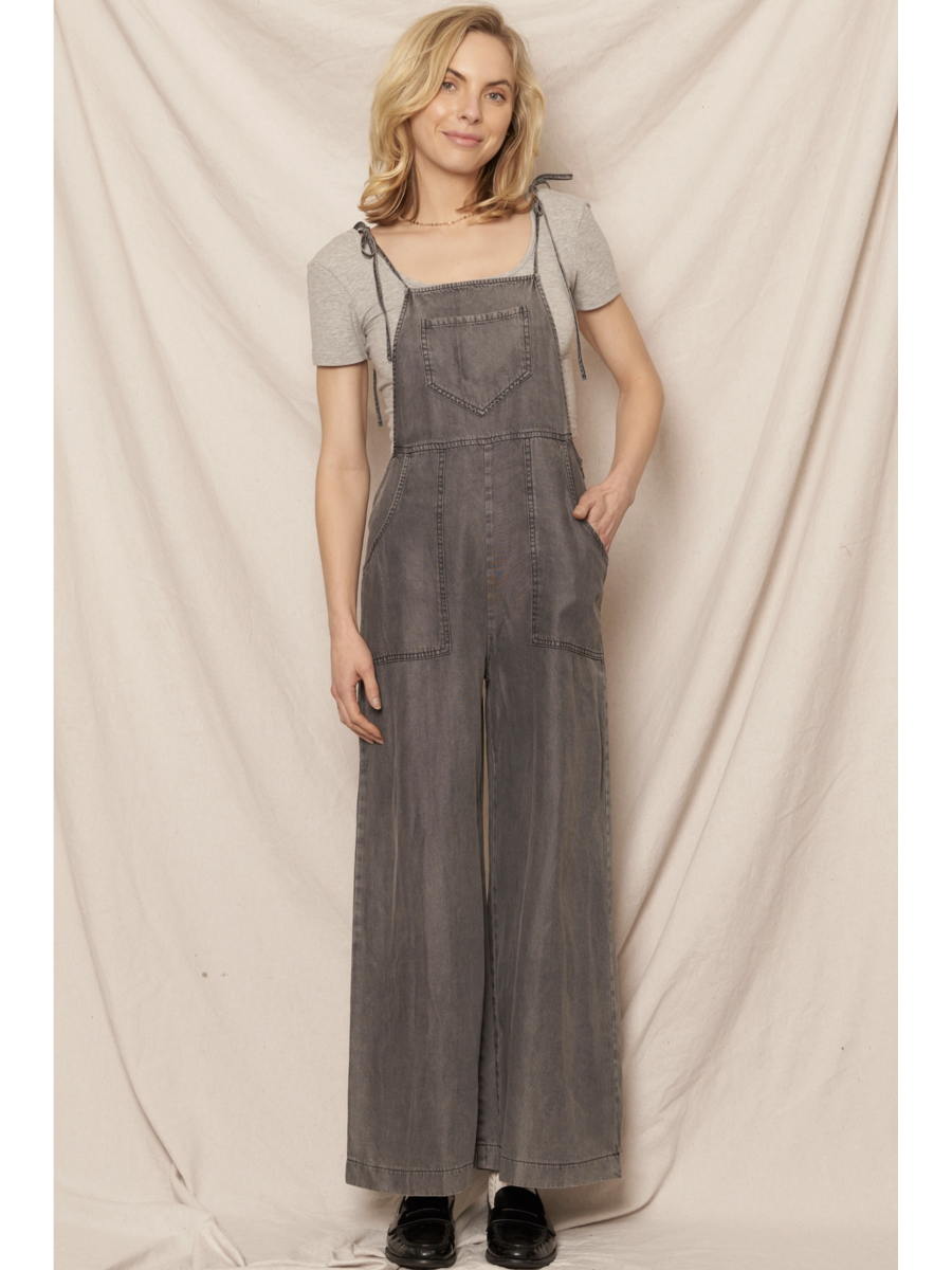 Black soft denim jumpsuit featuring adjustable tie shoulder straps, a square neckline, and a breezy wide-leg silhouette on a model.