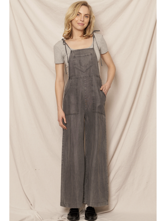 Black soft denim jumpsuit featuring adjustable tie shoulder straps, a square neckline, and a breezy wide-leg silhouette on a model.