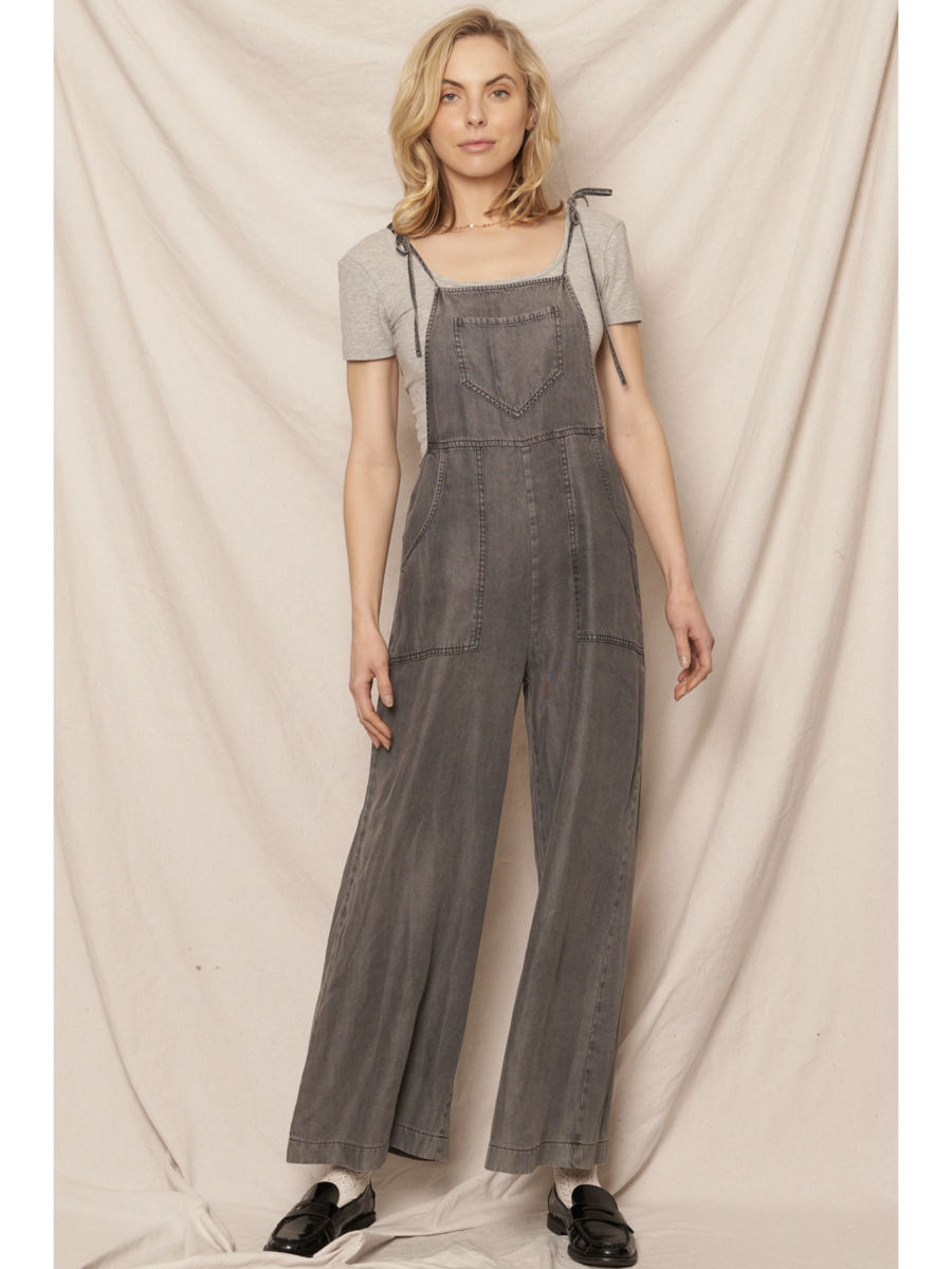 Black soft denim jumpsuit featuring adjustable tie shoulder straps, a square neckline, and a breezy wide-leg silhouette on a model.
