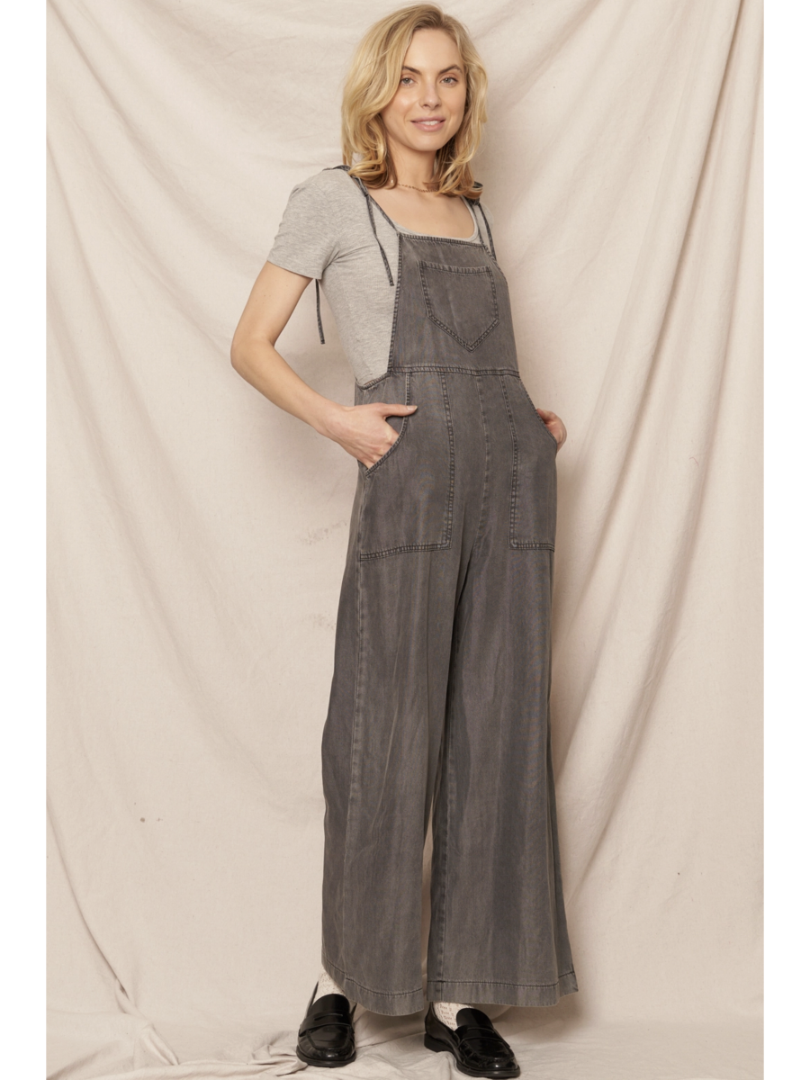Black soft denim jumpsuit featuring adjustable tie shoulder straps, a square neckline, and a breezy wide-leg silhouette on a model.