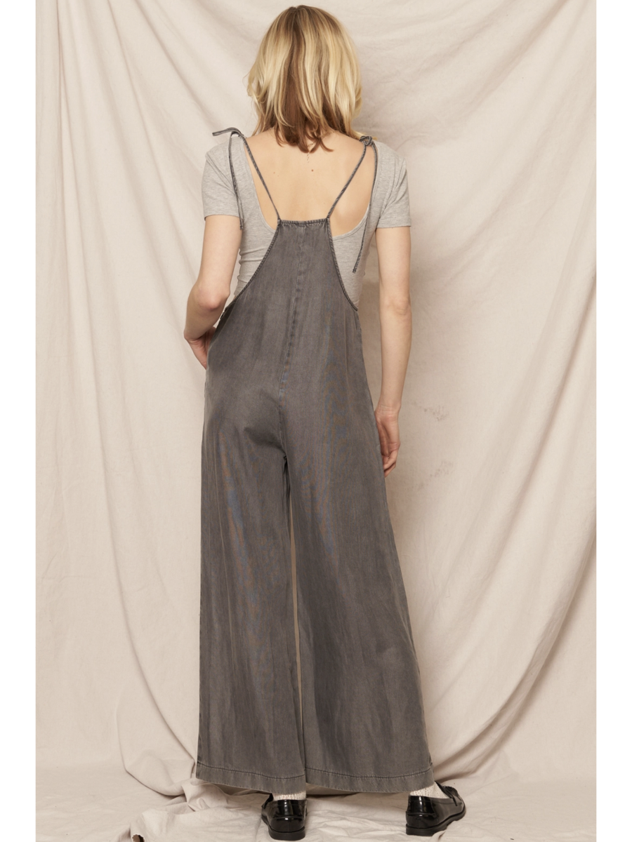 Black soft denim jumpsuit featuring adjustable tie shoulder straps, a square neckline, and a breezy wide-leg silhouette on a model.