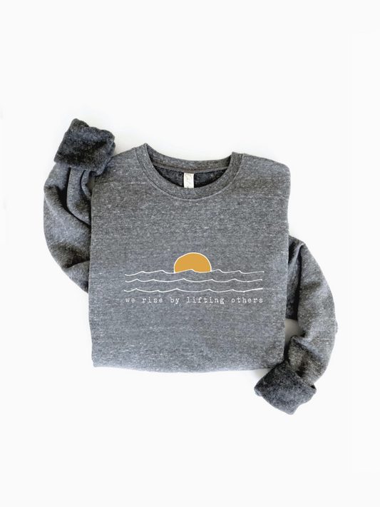 Shop our 'We Rise By Lifting Others' Sweatshirt. A whimsical, artisanal graphic pullover for slow living.