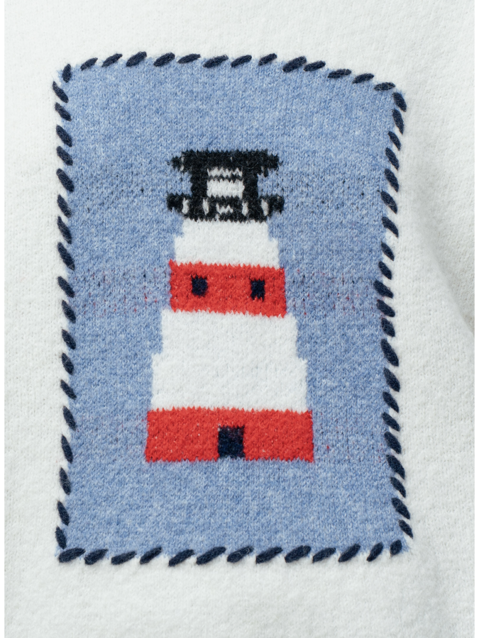 A woman wearing a cream knit sweater featuring a blue and white lighthouse design and blue whipstitch trim on the collar, cuffs, and bottom hem.