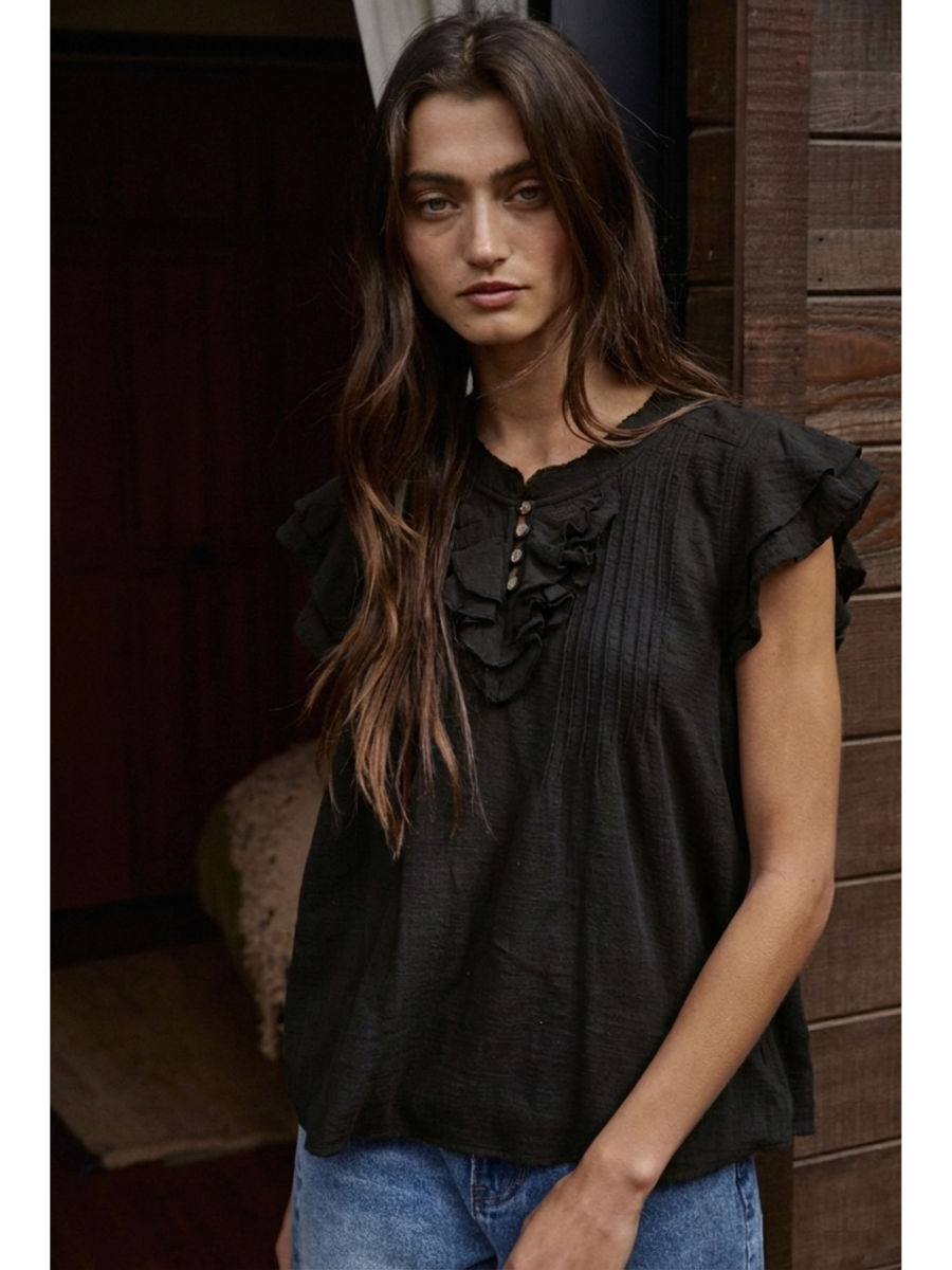 Woman wearing a Black cotton-linen blouse featuring a ruffled V-neckline, button-front, pin-tuck pleats on the chest, and tiered flutter sleeves.