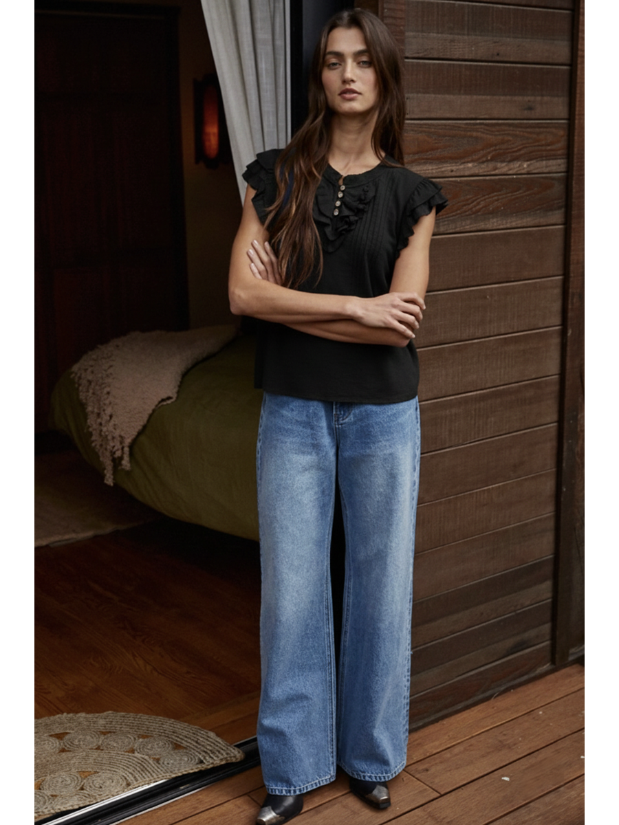 Woman wearing a Black cotton-linen blouse featuring a ruffled V-neckline, button-front, pin-tuck pleats on the chest, and tiered flutter sleeves.