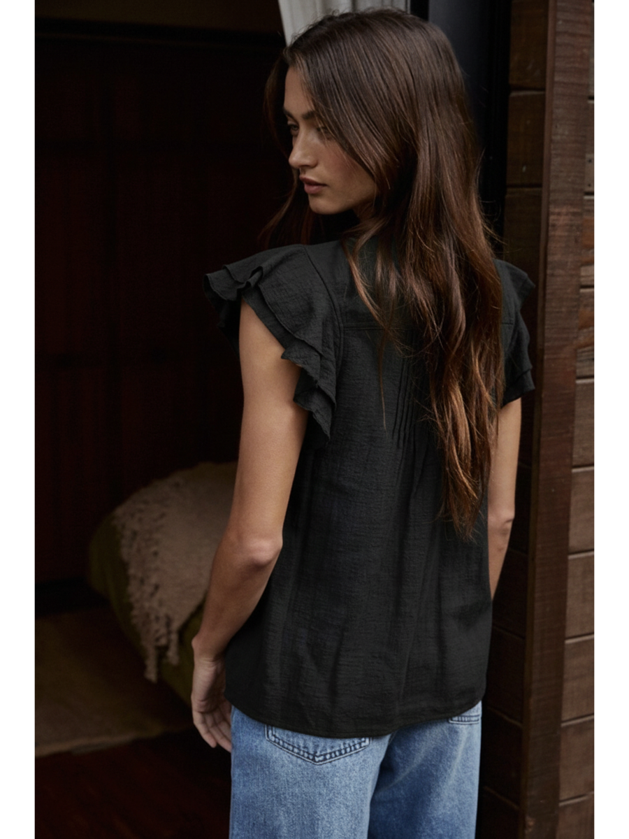 Woman wearing a Black cotton-linen blouse featuring a ruffled V-neckline, button-front, pin-tuck pleats on the chest, and tiered flutter sleeves.